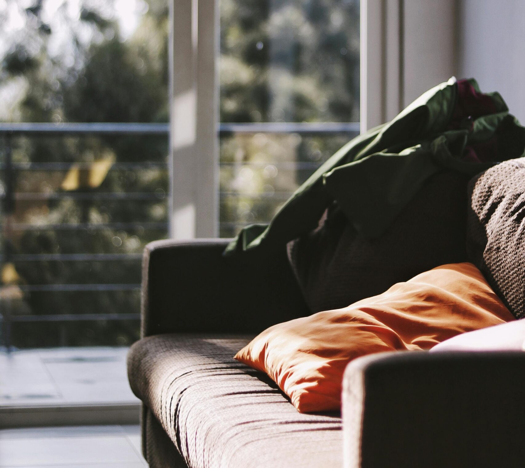 A cozy living room with sunlight streaming through sliding doors and soft cushions on a sofa.